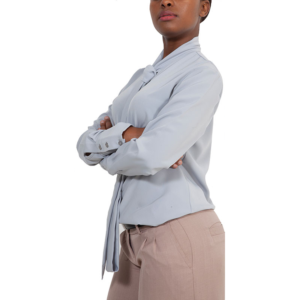 Professional woman in light blue tie-neck blouse and tan trousers, arms crossed, side view.