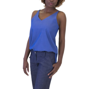 Professional woman in a royal blue V-neck sleeveless top and dark trousers, left hand in pocket, standing against a white background.