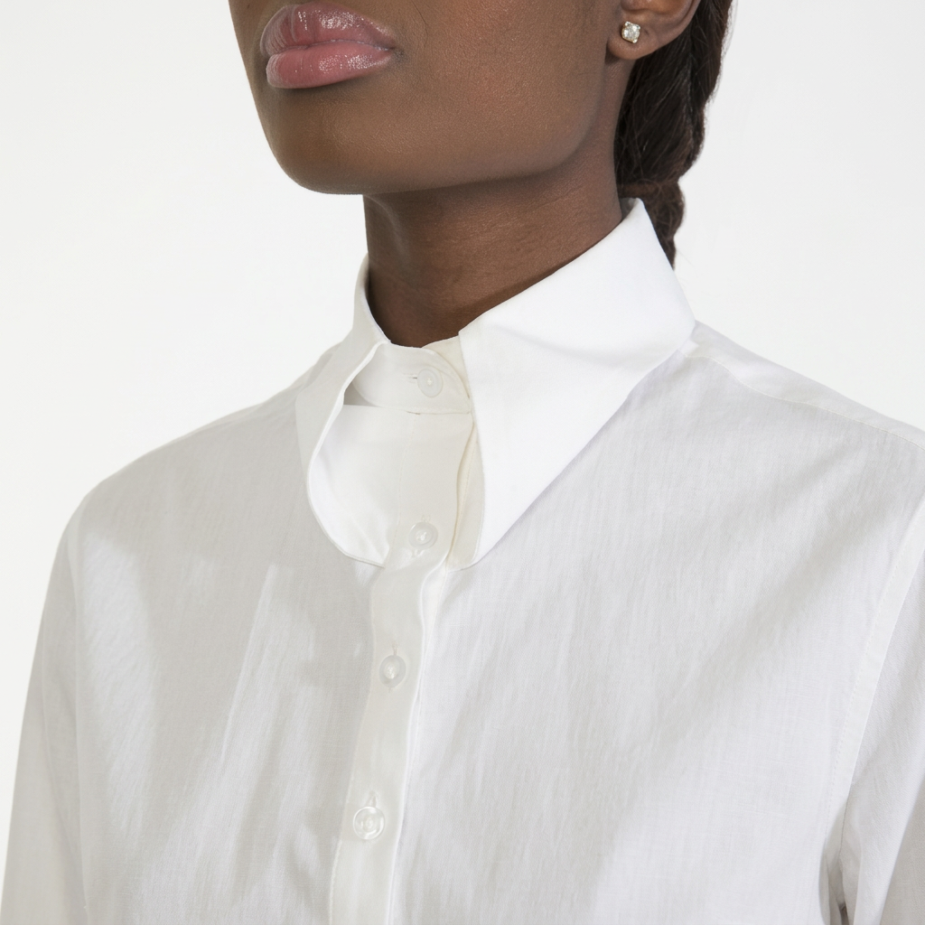 Radiant person with dark skin, glossy nude lips, and a delicate earring, in a white shirt with a stylized overlapping collar.