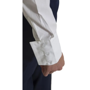 A close-up of a person’s arm wearing the Kuma Shirt 30, a white dress shirt with French cuffs fastened by clear buttons. The arm is relaxed by their side, with a dark garment visible in the background.