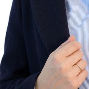 Close-up of a hand with a gold ring holding a dark blue jacket lapel over a pinstriped shirt.