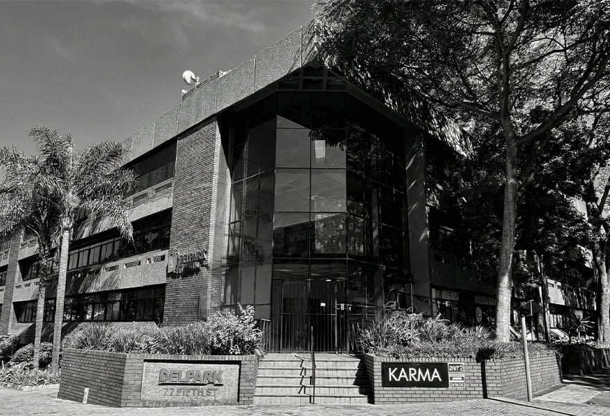 Modern commercial building housing Karma Clothing retail store in South Africa, featuring glass facade, lush landscaping, and urban architecture. Ideal for fashion shopping and retail experiences.