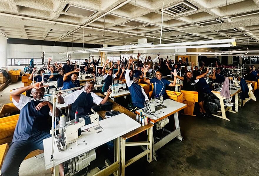 Colourful team at Karma Clothing 2.0 factory, showcasing diverse staff celebrating success in the clothing manufacturing industry. Modern, vibrant workspace with sewing stations and happy employees.