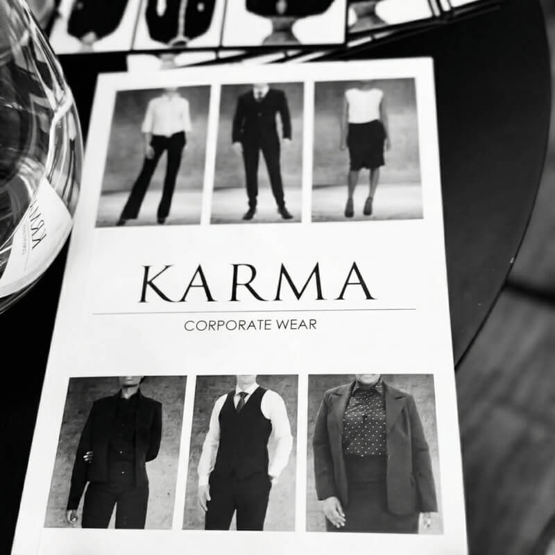 KARMA CORPORATE WEAR brochure, six B&W photos of models in corporate apparel, partially obscured by a wine glass.