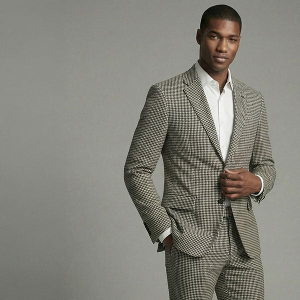 Man in a brown and white houndstooth suit and white shirt, standing with hand on lapel and in pocket.