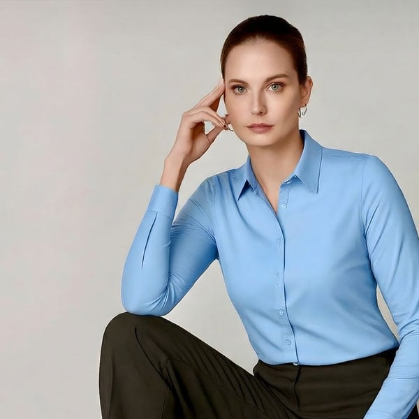 Professional woman in light blue button-up shirt, dark pants, looking at viewer, right hand to temple, thoughtful.